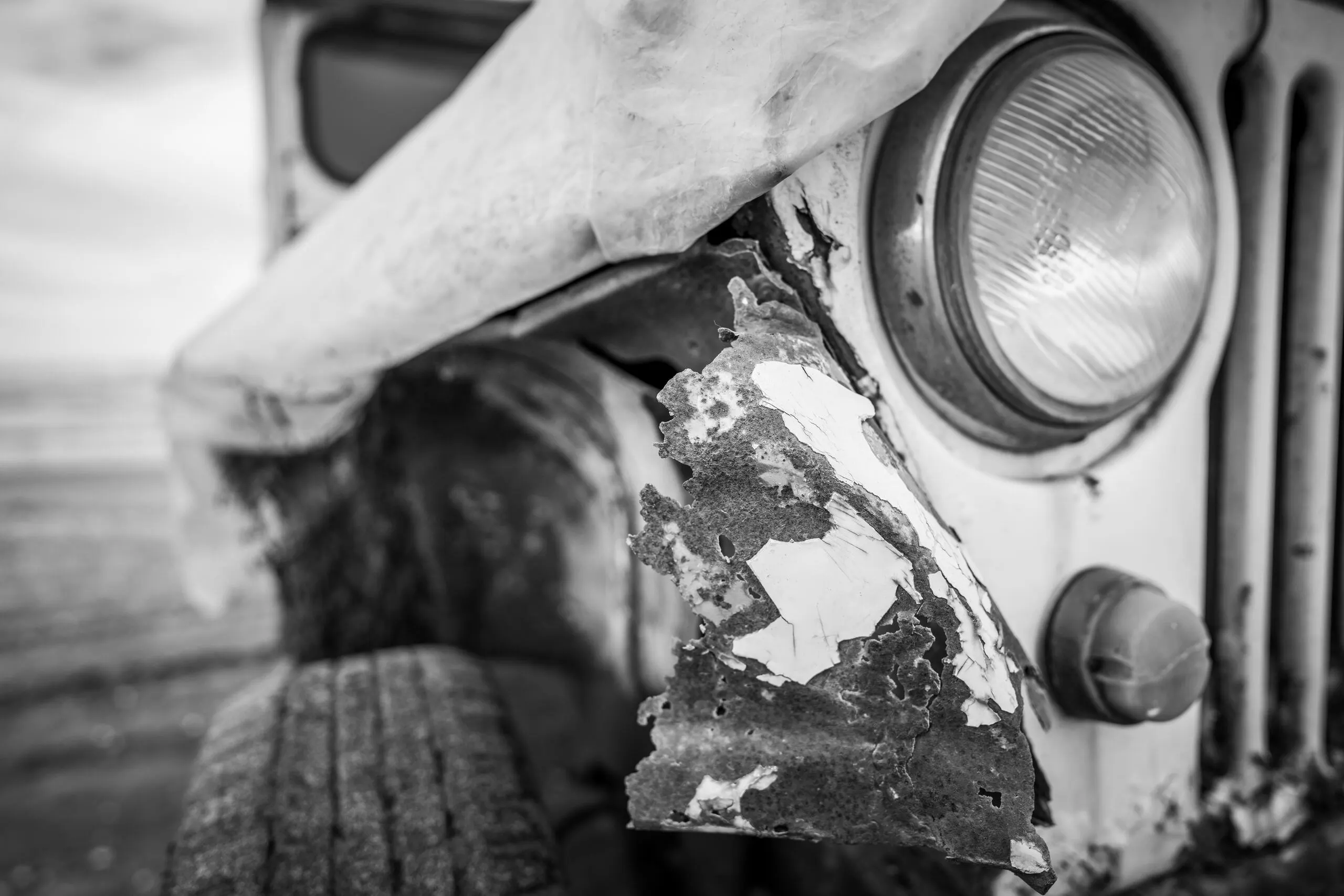 Close-up view of a dilapidated junk car with a visible headlight.